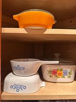 Orange Pyrex casserole on upper shelf, Corning Ware pieces below