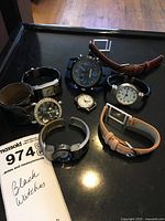 Group shot of all nine watches and two straps on black surface