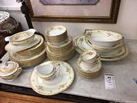 Full set stacked on marble surface showing plates, bowls, cups, serving pieces