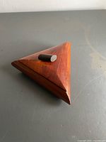 Closed triangular wooden box showing lid and handle