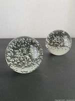 Two clear bubble art glass spheres on black surface