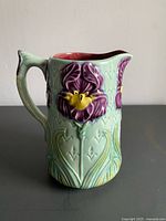 Front view of pale green majolica pitcher with purple and yellow iris relief