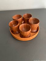 five teak egg cups arranged on round tray