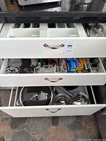 Three open kitchen drawers showing cutlery, small wares, packaged wraps and cookware