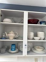 Cabinet view showing teapot, bowls, colored glassware and plates