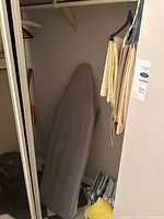 Closet view showing ironing board, table linens and assorted hangers