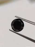 Close-up of front facet pattern of round black diamond held by tweezers