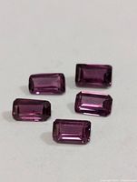 Five rectangular faceted garnet gemstones placed on a light surface