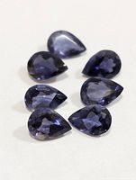 Seven pear-cut bluish-violet iolite gemstones on light background