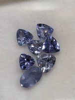 Seven loose faceted tanzanites on light background showing shapes and colour