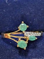 Front view of silver ring showing emerald stones and clear accents