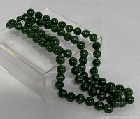 Full view of jade bead strand coiled on acrylic stand