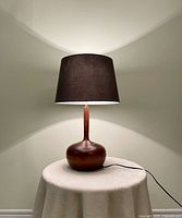 Full view of wooden lamp lit, showing base, neck, shade and cord