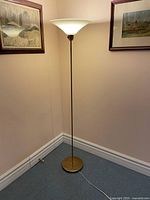 Full view of brass torchiere floor lamp lit, showing base, pole, shade and cord