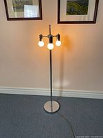 Full view of lit three-bulb chrome floor lamp.