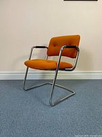 Front angle showing overall chair design, orange upholstery and chrome frame