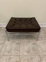 Front view of brown leather tufted ottoman on chrome frame