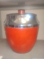 Front view of orange ice bucket with chrome band and lid
