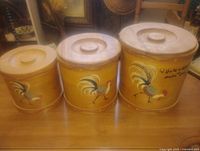 front view of three wooden rooster canisters showing lids and artwork