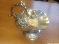 Side view of silver plated sugar scuttle and scoop showing etched floral design and pedestal base