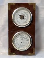 Full view of wooden weather station showing two gauges and brass corners