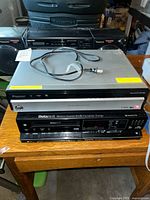 Front view showing GE DVD player stacked over Sanyo Betacord VCR; Panasonic boombox and Pioneer receiver visible behind