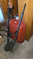 Full view of wheelbarrow showing red steel tub, black frame, pneumatic wheel