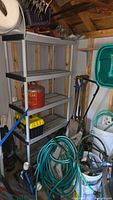Wide view showing shelf with red gas can, toolbox, shovels, snow shovel, hoses on reel, hose accessories