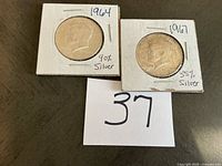 Two Kennedy Half Dollar coins in holders with handwritten dates and silver content