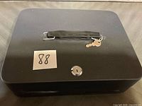 Closed black cash box showing handle, lock and key