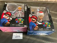 Front view of both boxed figures side by side, lot number card visible