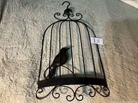 Full view of metal birdcage wall hanging showing scrollwork and interior bird