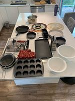 Overview of cookware, bakeware, serving plates, mixing bowls, utensils laid on countertop