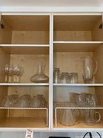 Cabinet shelves showing wine glasses, tumblers, decanter, pitcher, handled cups