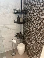 Corner shower showing black rack, toilet paper holder, trash bin