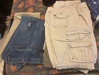 Stack of khaki cargo shorts, olive pants and denim pants on bed