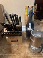 Knife block with 27 black-handled knives beside packaged skewers, grill brush and NutriBullet base