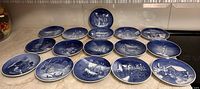 Sixteen blue and white Bing & Grondahl Christmas plates laid out showing front designs