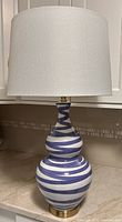 Full view of blue and white striped ceramic table lamp with white drum shade on countertop