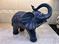 Left side view of navy blue glazed ceramic elephant displaying ornate swirl relief and raised trunk