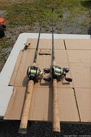 Two casting rods with attached baitcast reels laid on cardboard