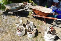 two steel wheelbarrows and five buckets of tools outdoors