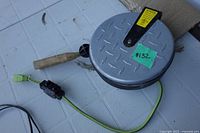 Full view of grey metal cord reel with green cord, outlet block and wooden crank handle