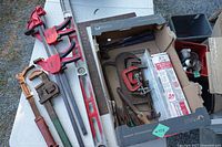 Tabletop view of bar clamps, level, pipe wrench, squares alongside box of tools