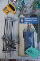 Sealed 12V chainsaw sharpener package beside metal clamp with file