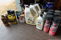 All containers of motor oil, brake fluid, transmission treatment, tire sealant and six undercoating cans arranged on table