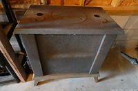 Front/side view of rectangular stove body, top with three circular lids, rust visible
