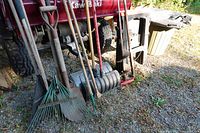group of yard tools leaning against vehicle including rakes, shovels, ice auger