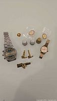 Overview showing two wristwatches, three thimbles, cufflinks, tie clip and pins