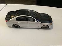 Driver side profile of BMW M5 model showing white body, black hood/roof/trunk, wheels